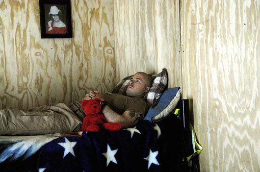 A helicopter medic waits in his ready hut in Baghdad for a call to action. His girlfriend had sent him the teddy bear for good luck. He had another one hanging next to his carbine on the chopper.